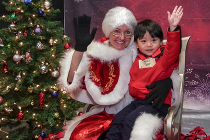 Small child waving with Mrs. Claus in front of a Christmas tree