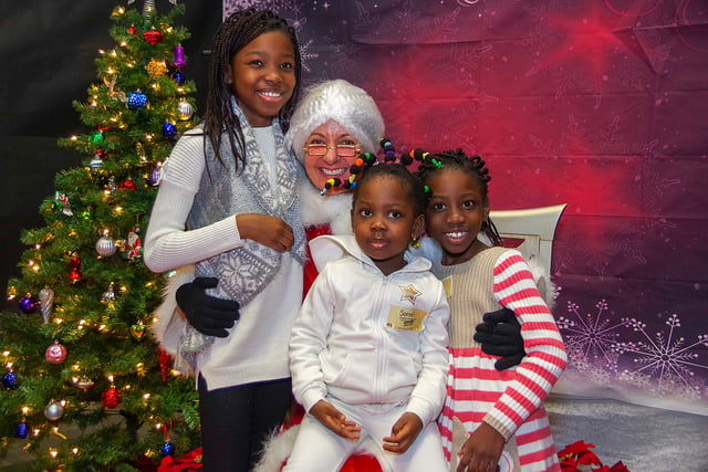 Three young girls posing in front of a Christmas Tree with Mrs. Claus