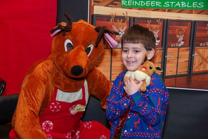 Young boy hugging a stuffed animal and posting with someone in a reindeer costume