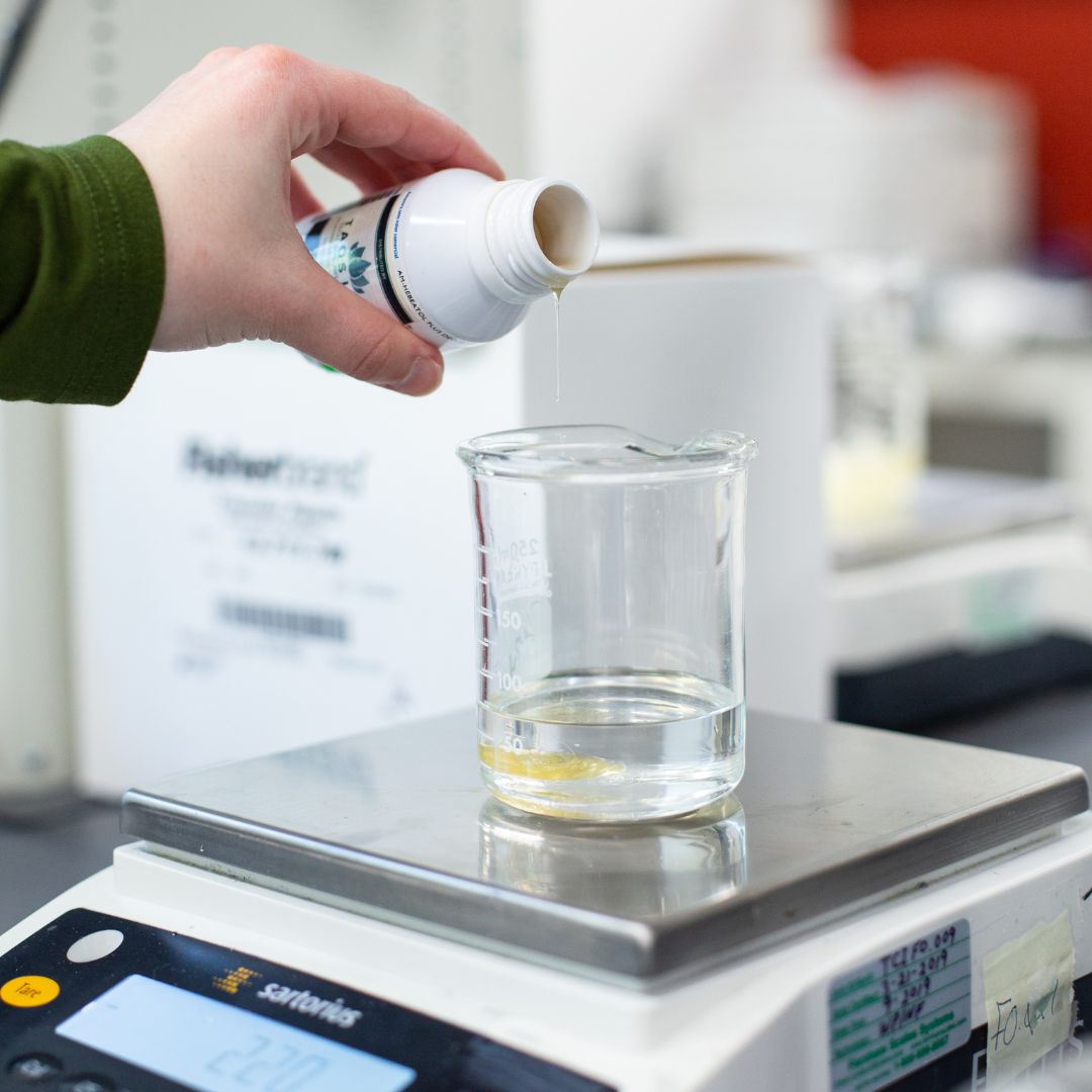 Twincraft employee pouring a raw material into a beaker in our lab