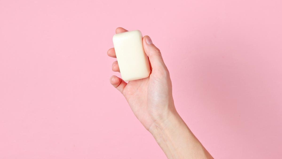 hand-holding-bar-of-soap-pink-background